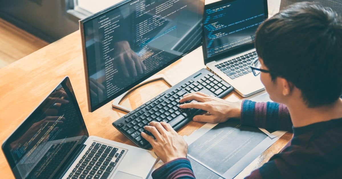 A man sitting at a desk with two laptops in front of him, focusing on automation testing technologies.