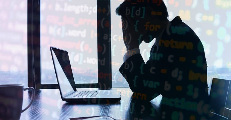 Silhouette of a software developer working on a laptop with overlapping digital code.