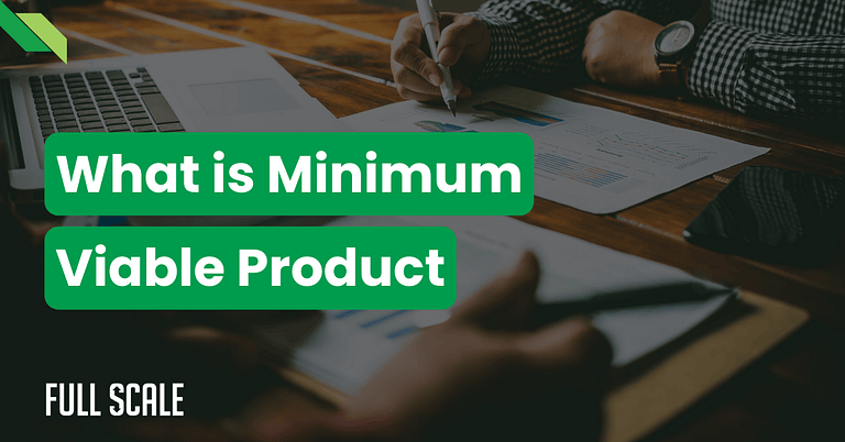 Two people sit at a wooden table with papers and a laptop, overlaid text reads: "What is a minimum viable product definition.