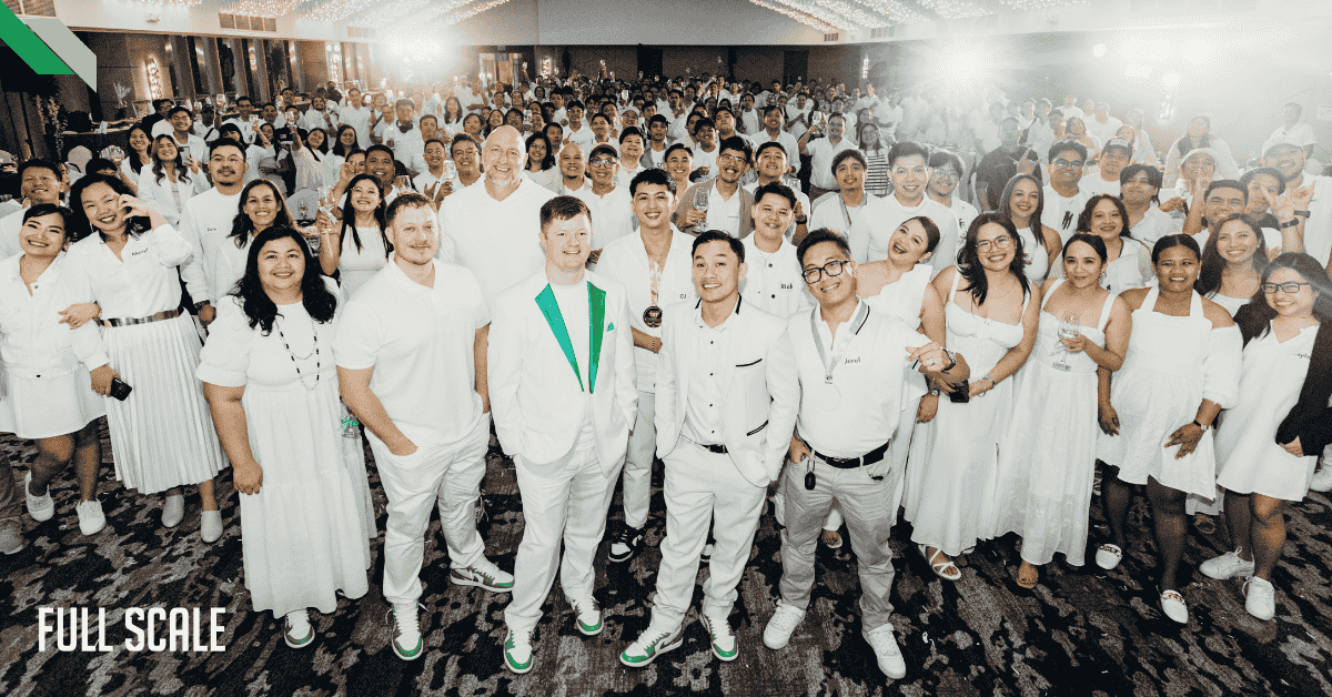 A large group of people dressed in white pose together in a well-lit room with a patterned carpet.