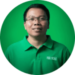 A man wearing glasses and a green collared shirt with "REAL ESTATE" text stands in front of a green background, facing the camera and smiling.