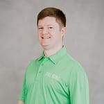 A person in a green polo shirt smiles against a gray background.