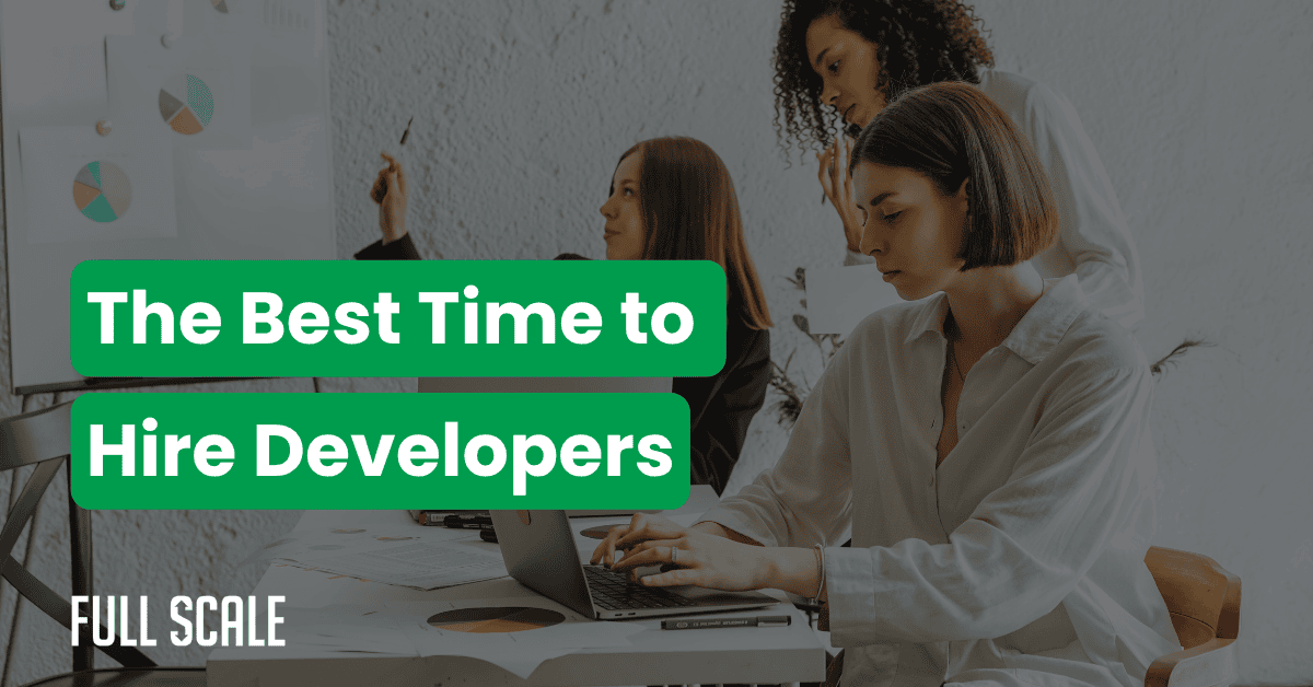 Three women work together at a desk with laptops and documents. A chart on the wall highlights the best time to hire developers. Text reads: "The Best Time to Hire Developers. Full Scale.